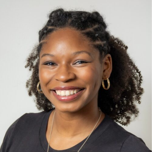 Maya Jacobs, a Black woman with hoop earrings in a Black tshirt smiles at the camera